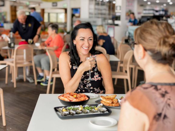 mooloolaba-surf-club-smiling-woman-holding-wine-prawns-and-oysters