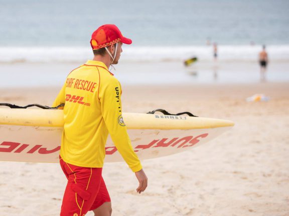 mooloolaba-surf-club-surf-lifesaving-member-with-board-on-beach